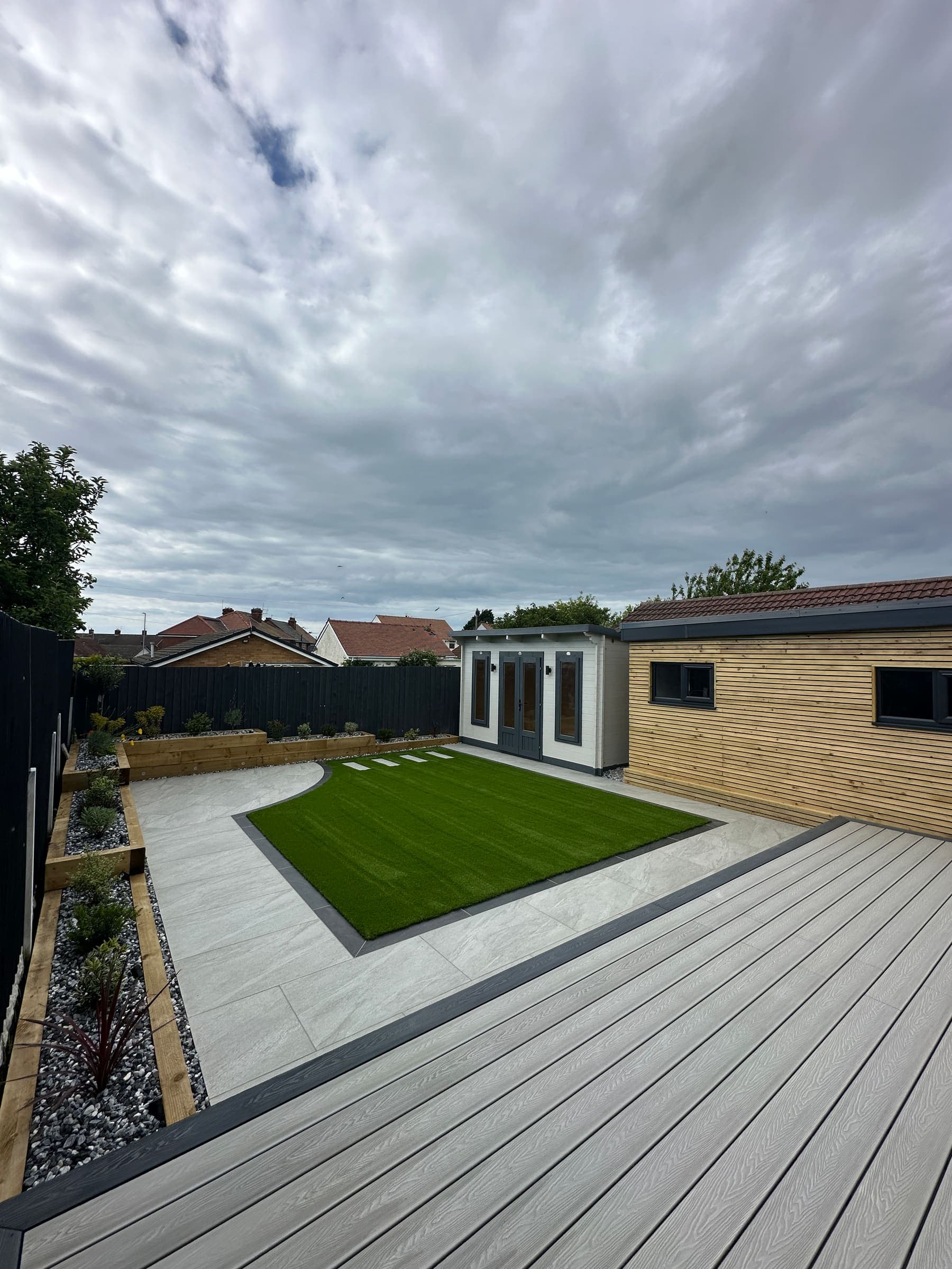 Modern Liverpool garden with artificial grass, porcelain paving, composite decking and an insulated garden room