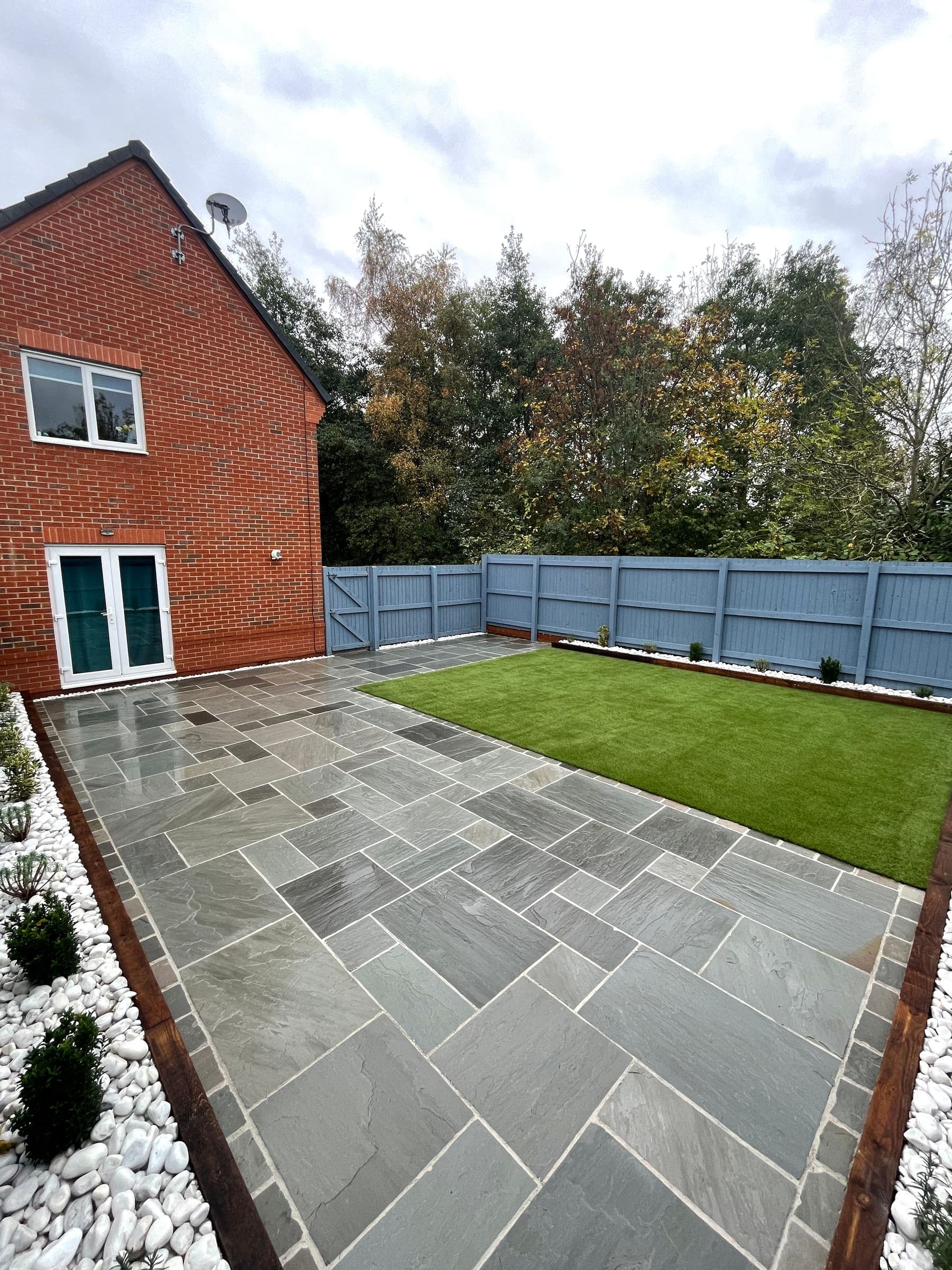 Modern patio installation in Liverpool with grey paving, artificial grass and a fenced garden