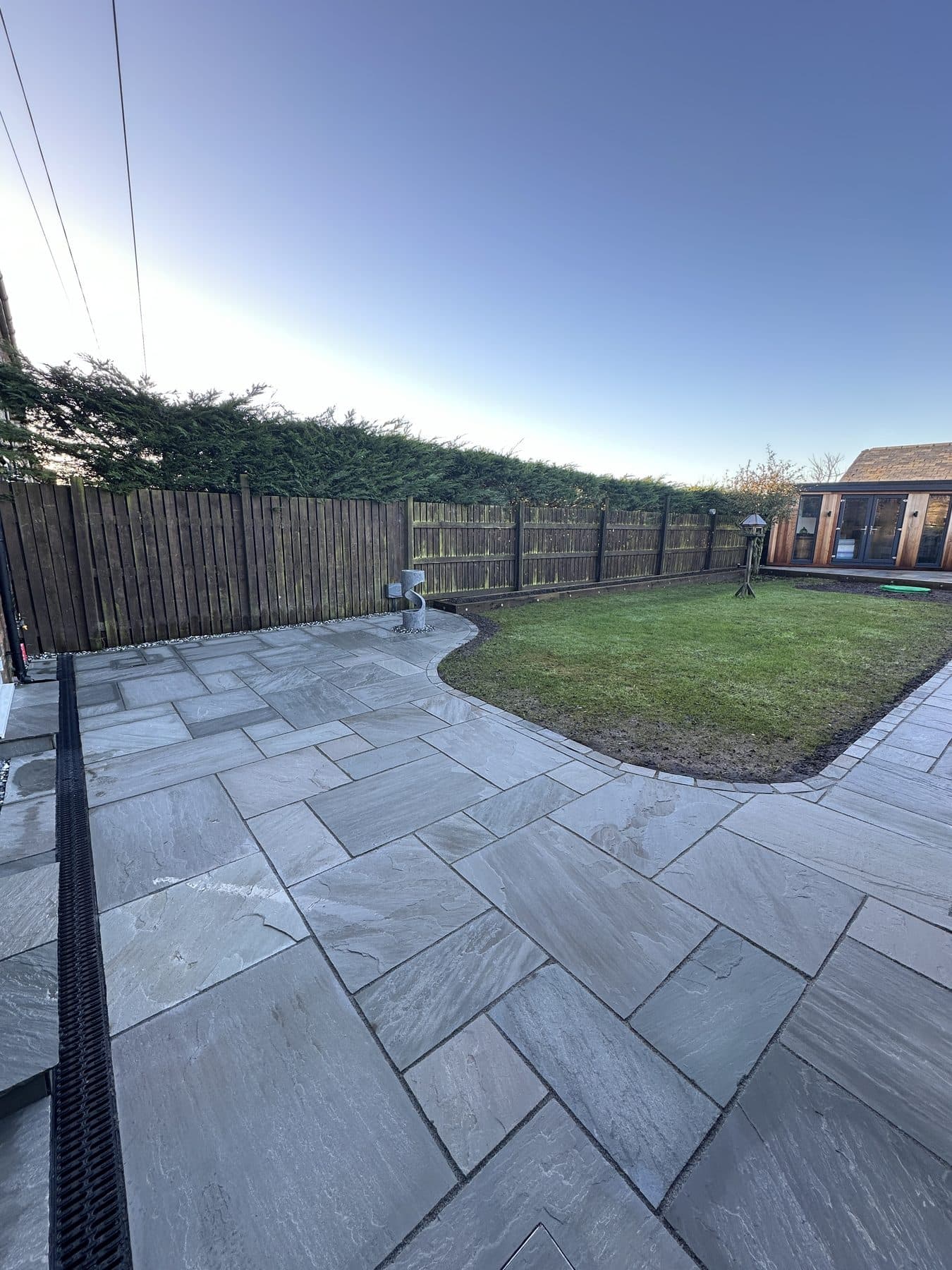 Grey sandstone patio with a curved lawn edge and drainage channel in a Liverpool back garden