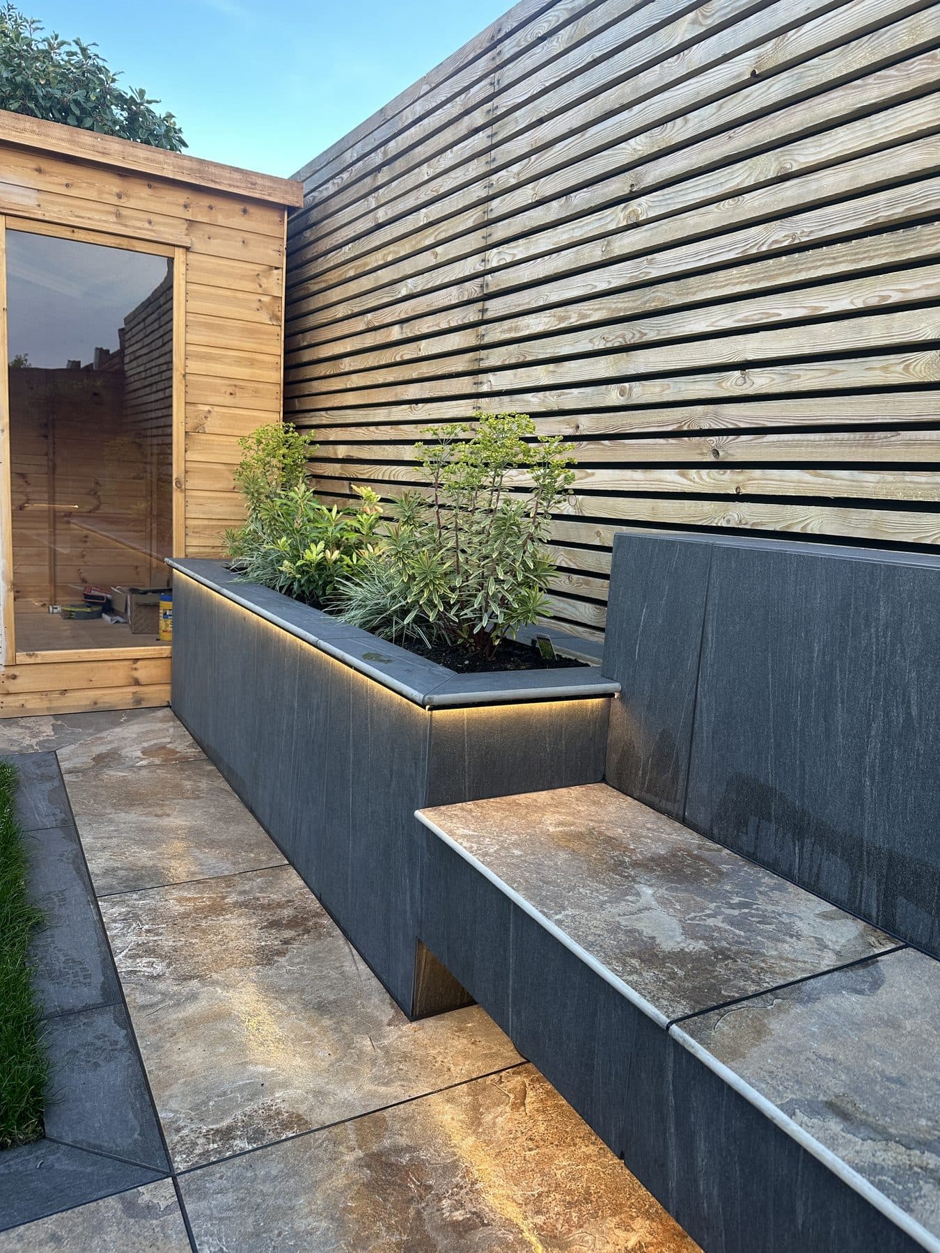 Porcelain raised planter with built-in lighting and a bench seat against a slatted fence in a Liverpool garden